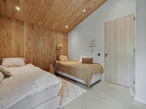 Ein Schlafzimmer mit zwei Betten, Holzboden, einer weißen Tür und einem kleinen Nachttisch.