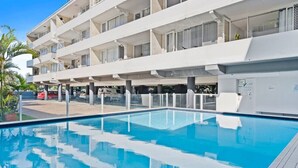 Ein modernes Hotel mit Schwimmbad, mehreren Balkonen und einem Parkplatz.
