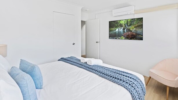 Ein modernes Schlafzimmer mit einem Bett, einem Sessel und einem an der Wand montierten Fernseher, der eine Naturdarstellung zeigt.