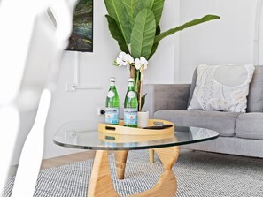 A modern living room with a glass coffee table, a grey sofa, and a large plant. - Beachfront Escape Broadbeach (Broadbeach)