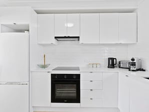 A modern kitchen with white cabinetry, a built-in oven, a coffee maker, and a toaster. - Beachfront Escape Broadbeach (Broadbeach)