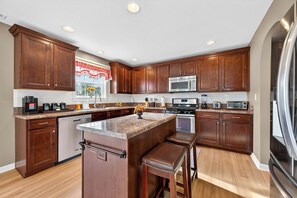 A modern kitchen with wooden cabinets, stainless steel appliances, and a central island with stools. - Roadmap Lodging: 3BR + Office, Loft, Fenced Yard (Columbus)
