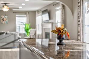 Une cuisine moderne avec un plan de travail en marbre, un vase décoratif contenant des feuilles séchées et une vue sur l’espace repas.