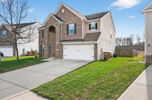 A two-story house with a brick facade, a garage, and a well-maintained lawn. - Roadmap Lodging: 3BR + Office, Loft, Fenced Yard (Columbus)