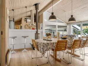 Cocina moderna con vigas de madera, zona de comedor con mesa dispuesta para cuatro personas y un amplio ventanal con vistas a un jardín.