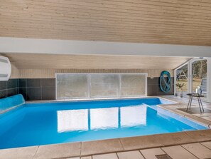 Una piscina con un borde de baldosas, un área techada con una ventana y una manguera a la derecha.