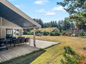 Un espacio al aire libre techado con una mesa y sillas, una parrilla de barbacoa y un césped con árboles al fondo.
