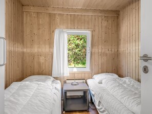 Eine kleine, einfache Unterkunft mit zwei Betten, einem Fenster mit Blick auf Grünflächen, einem Nachttisch mit Lampe und einer Tür mit Griff.