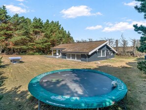 Ein Trampolin in einem Garten mit einem Haus und Bäumen im Hintergrund.