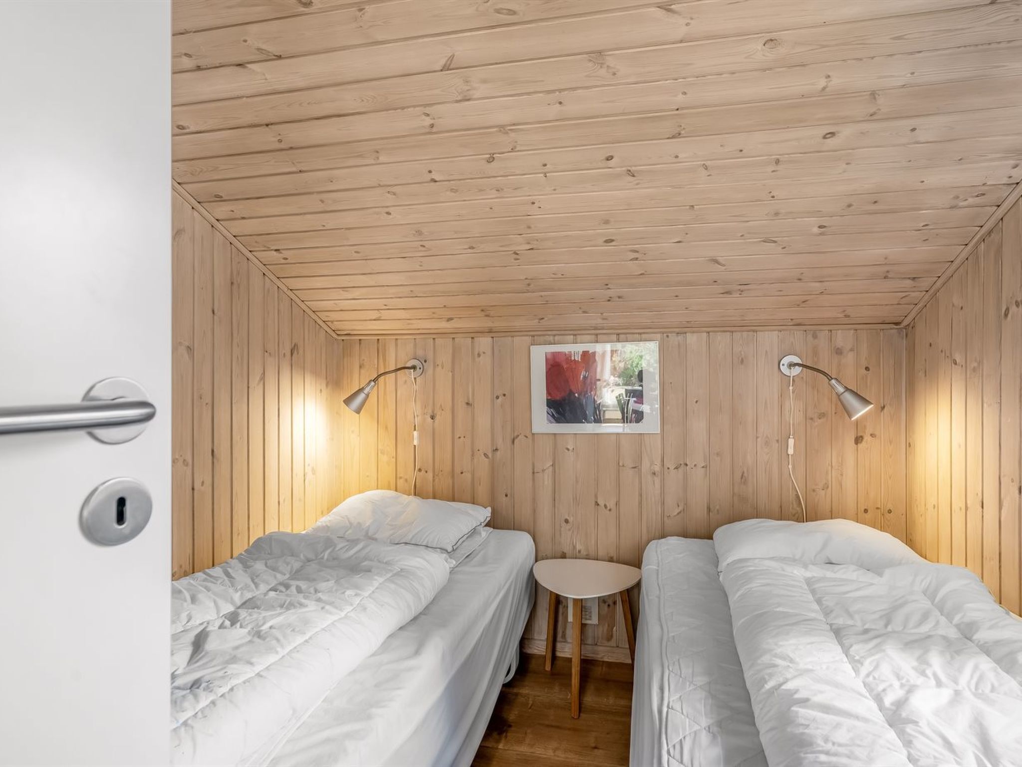 Habitación con dos camas, una mesita pequeña y paredes de madera.