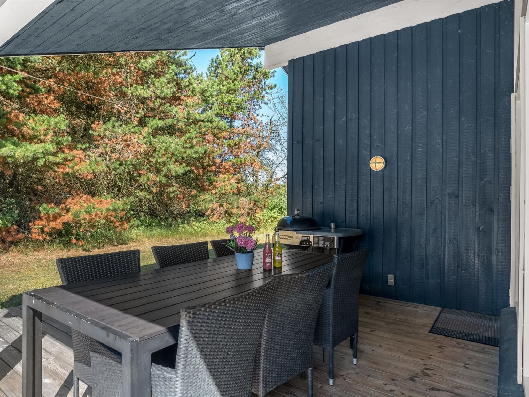 Ein Essbereich im Freien mit Holztisch und -stühlen, einem Grill und einem Blumentopf.