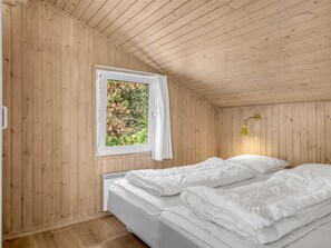 Une pièce aux murs en bois, un lit avec une literie blanche, une fenêtre avec un rideau et une lampe fixée au mur.