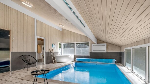 En modern inomhuspool med ett kaklat golv, en solstol och ett litet bord.