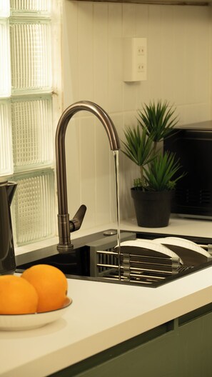 A kitchen with a modern faucet, a potted plant, and a bowl of oranges on the counter. - Studio with chill balcony: D3 Apt By D Haus (Thành phố Hồ Chí Minh)