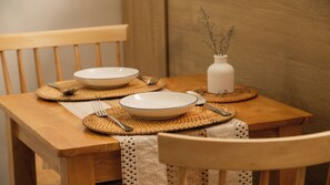 A wooden dining table with two white bowls, cutlery, and a white vase with dried flowers on woven placemats. - Studio with chill balcony: D3 Apt By D Haus (Thành phố Hồ Chí Minh)