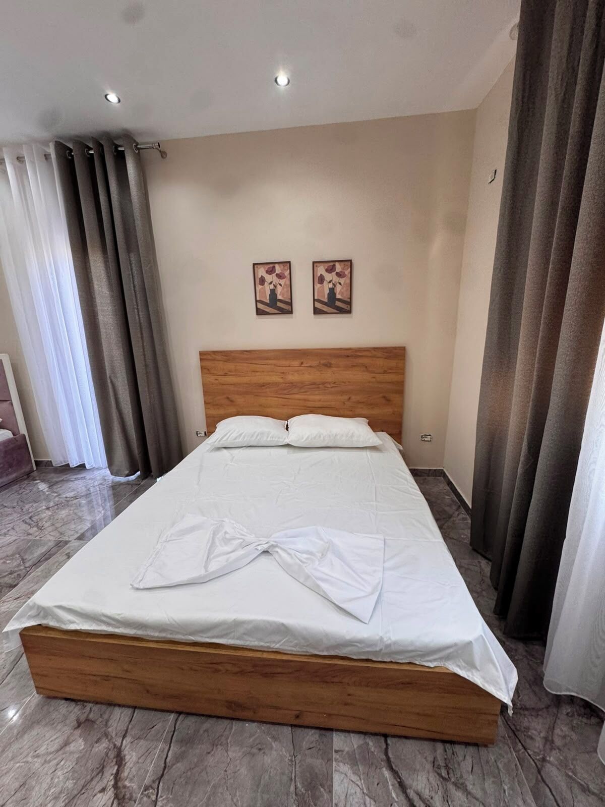 Un lit bien fait, avec une tête de lit en bois, deux tableaux accrochés au mur et un sol en marbre.