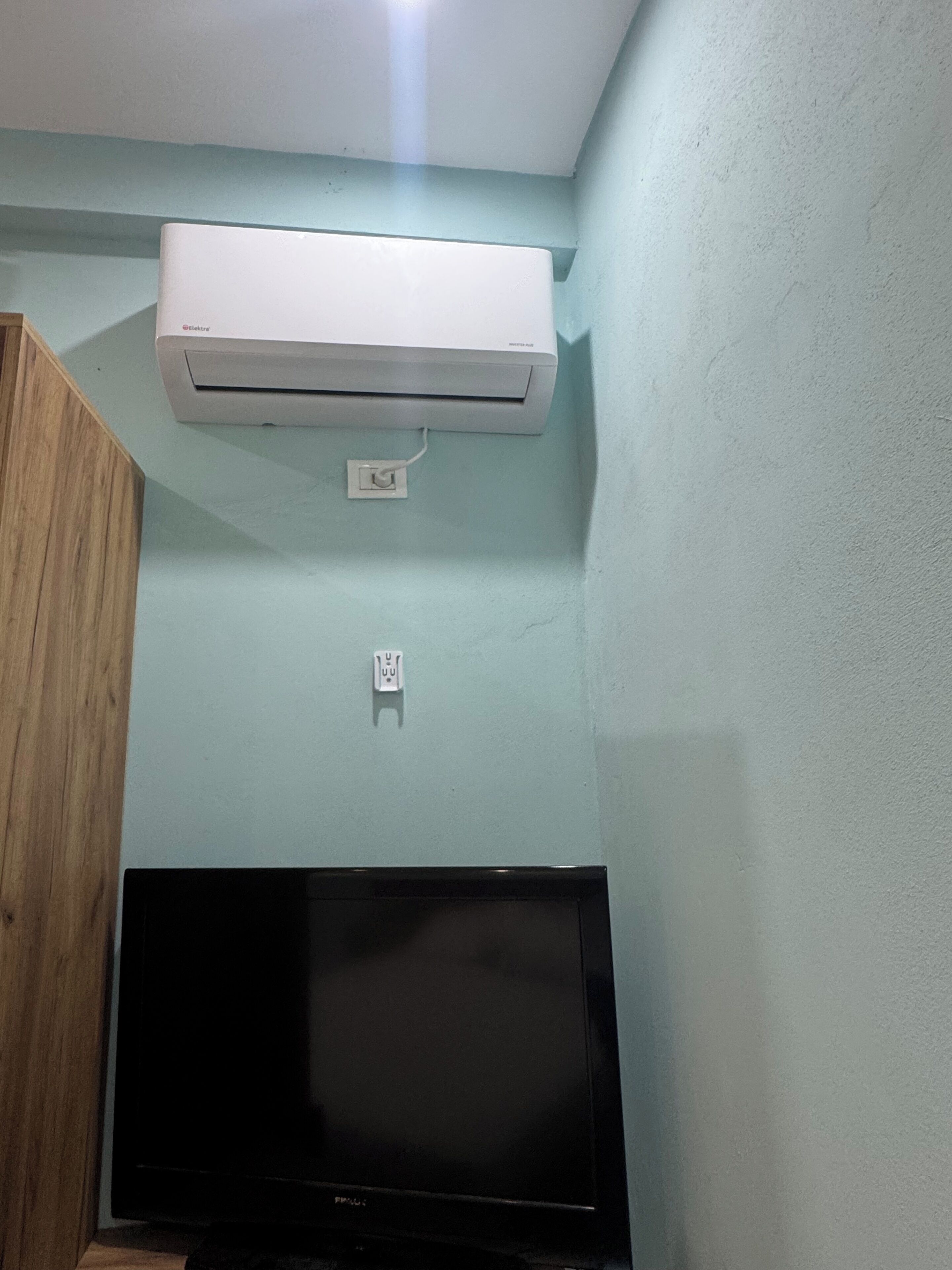 A room with a mounted air conditioner, a flat-screen TV, and a wooden cabinet.