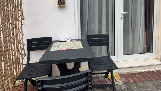 Un patio con mesa y sillas, un adorno en la pared y un ventanal corredizo.