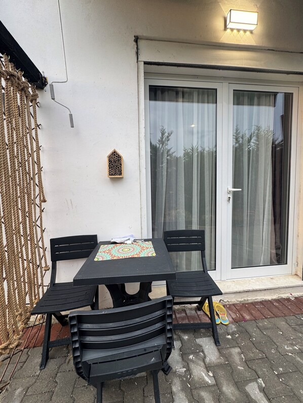 A patio with a table and chairs, a decorative wall piece, and a sliding glass door.
