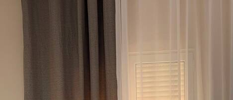 A bedroom with a bed, a window with blinds, and a curtain.