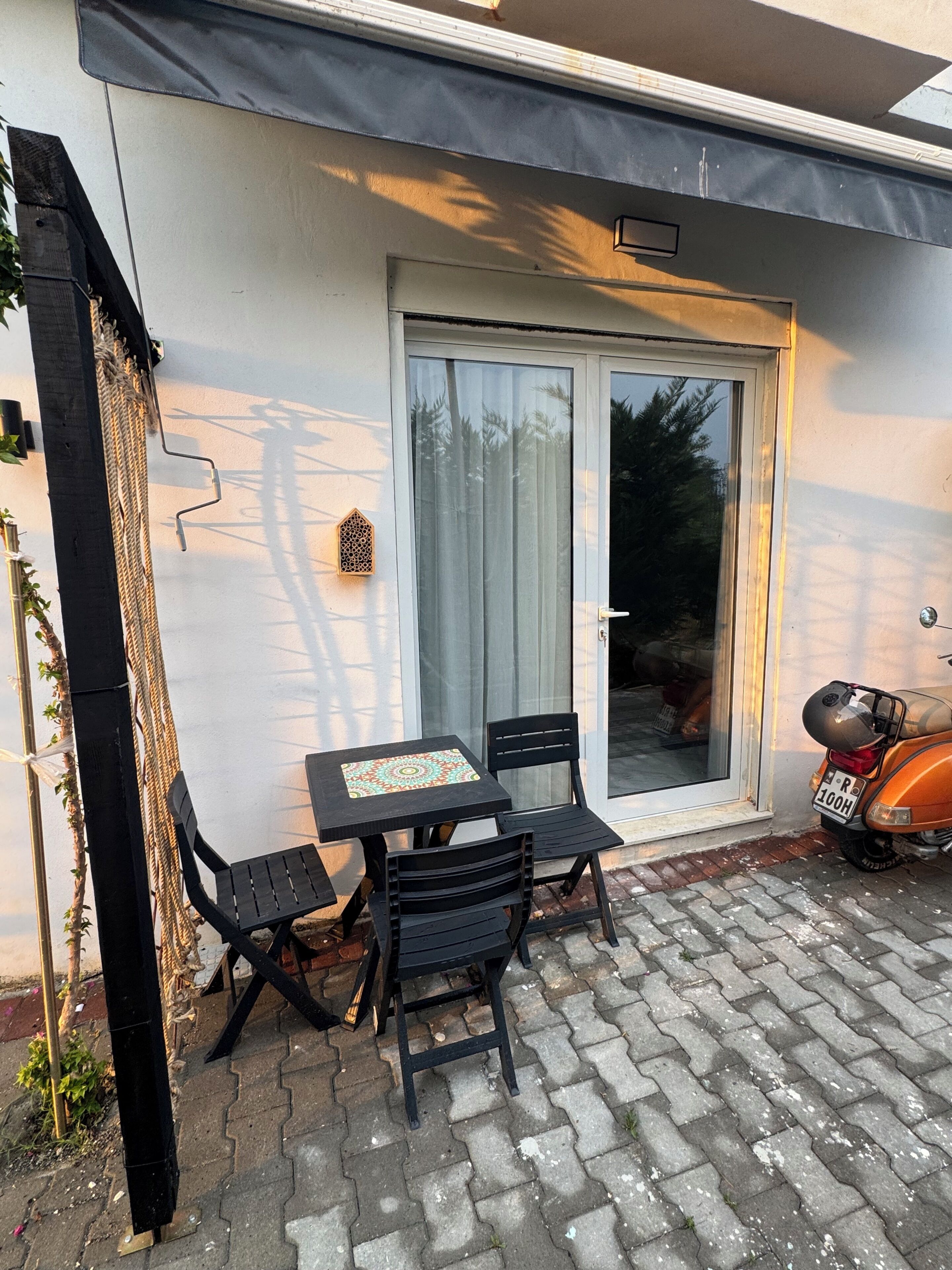 An outdoor seating area with a table and chairs, a scooter parked nearby, and a sliding glass door.