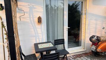 An outdoor seating area with a table and chairs, a scooter parked nearby, and a sliding glass door.