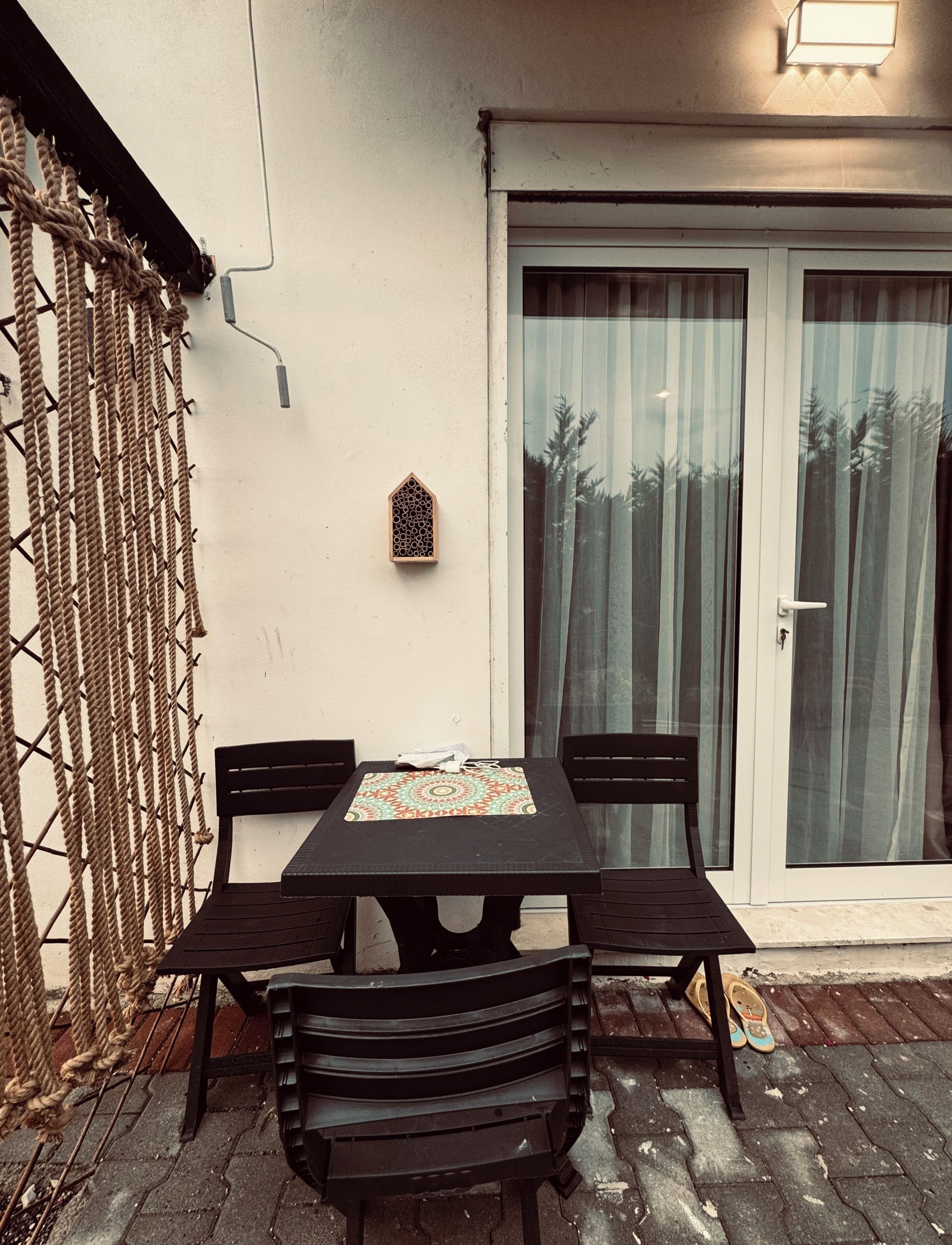 Une terrasse avec une table et des chaises, un élément décoratif mural et une porte-fenêtre coulissante avec des rideaux.