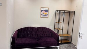 Una habitación con un sofá morado, una puerta blanca y un cartel enmarcado en la pared.