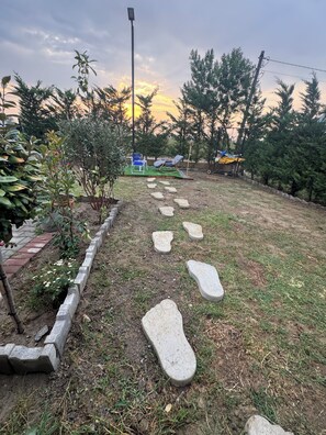A garden pathway with stepping stones leading to a seating area with a blue chair and a yellow umbrella. - Calm and Green Retreat (Velipojë)