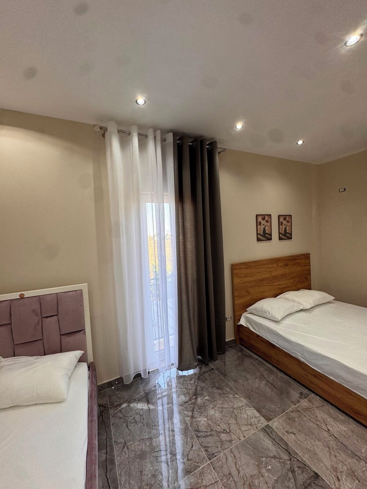 Una camera d'albergo con due letti, una testiera in legno, pavimento in marmo e una finestra con tende.