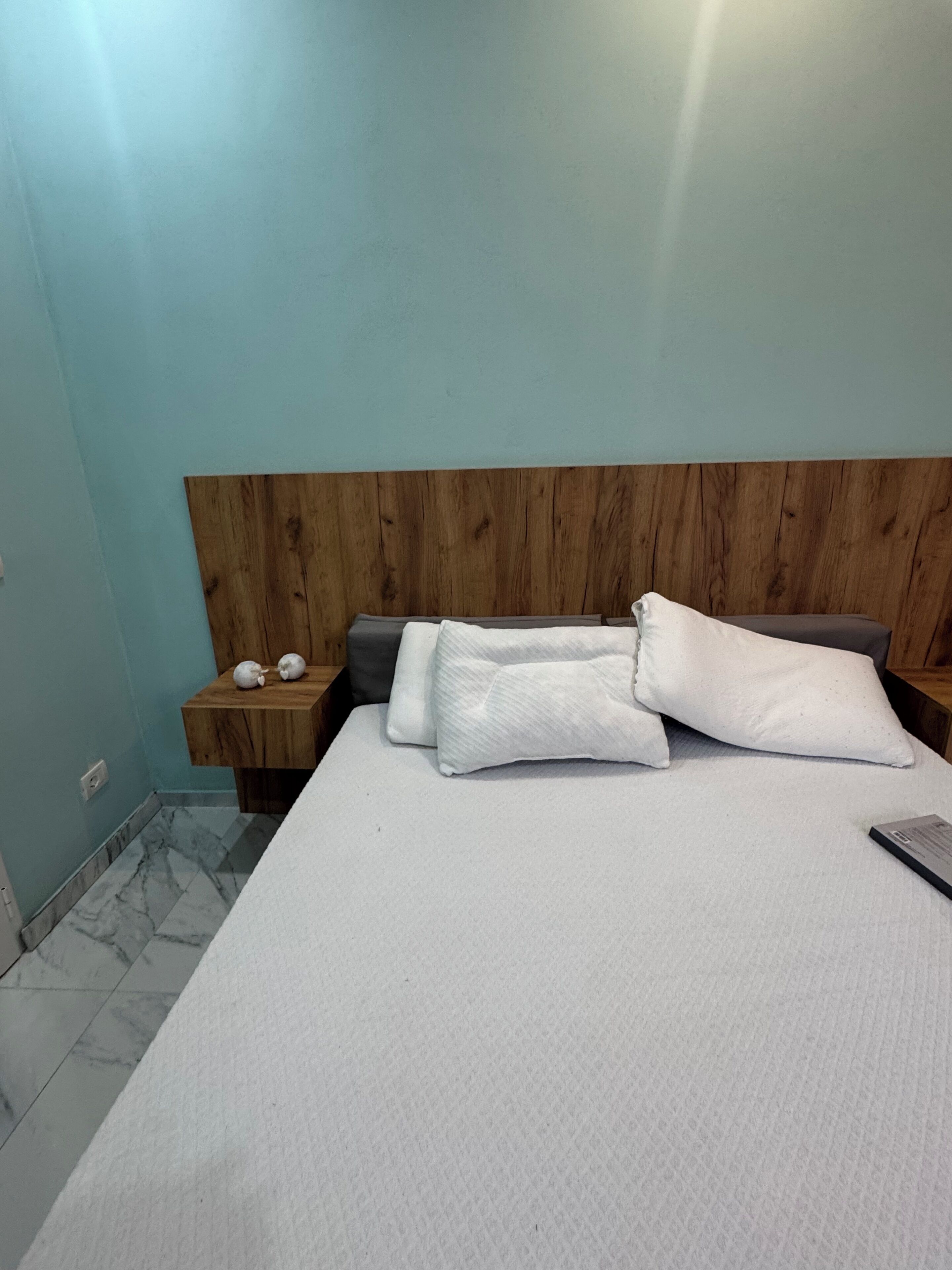 Un dormitorio con cabecera de madera, una cama con ropa blanca, dos mesitas de noche y un suelo con estampado de mármol.