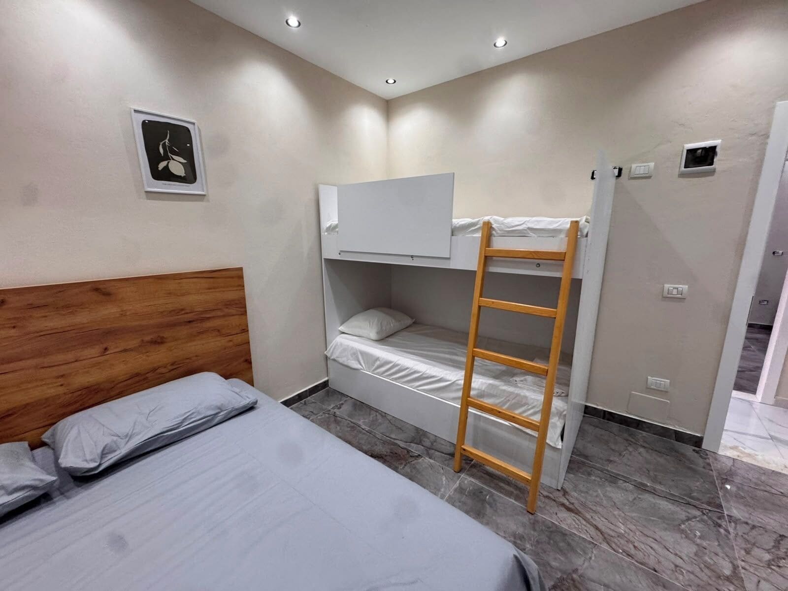 A bedroom with a bunk bed, a single bed, a wooden ladder, a white wardrobe, and a small picture on the wall.