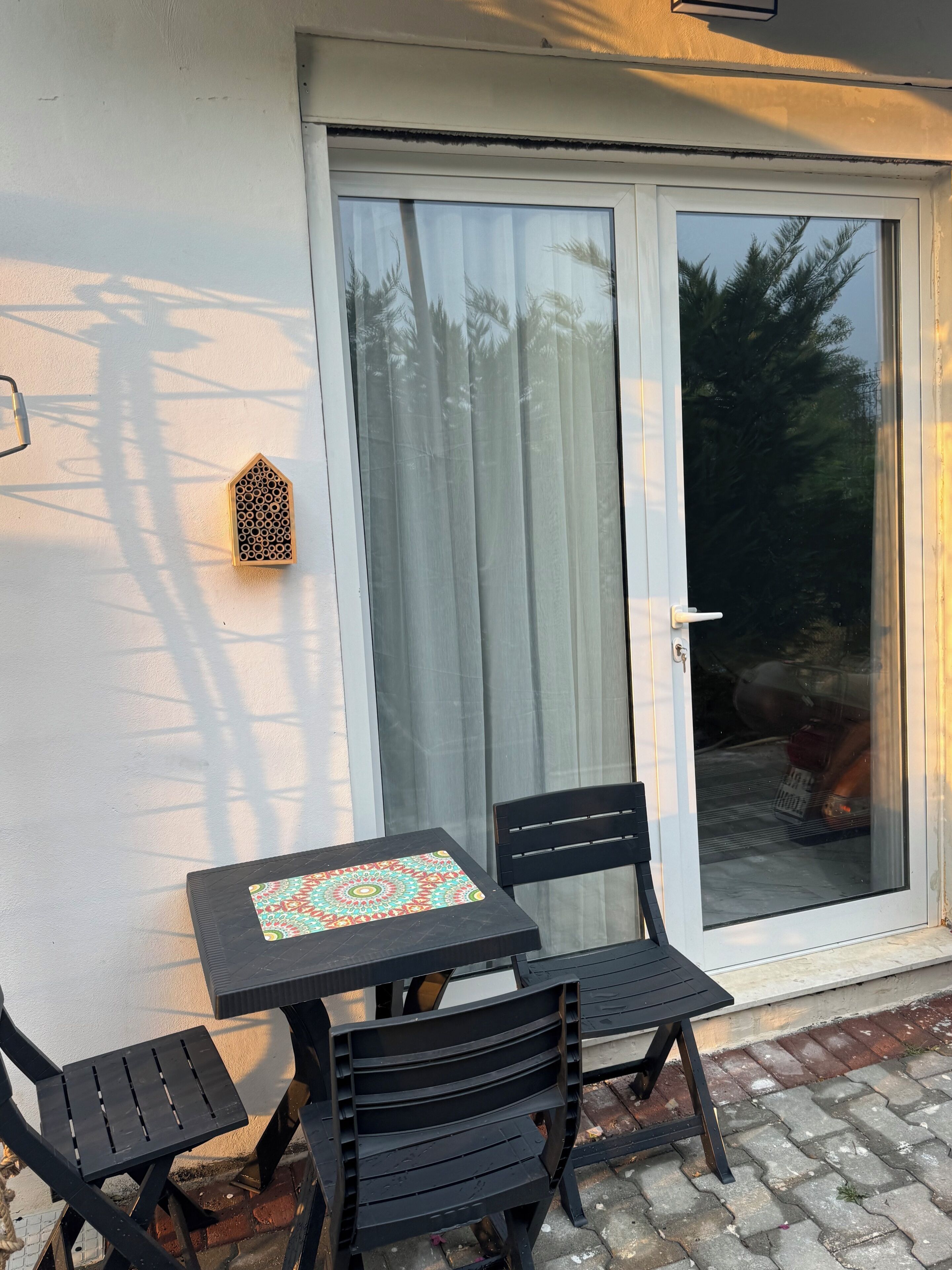 Une terrasse avec une table et des chaises, une porte-fenêtre coulissante et un élément décoratif mural.