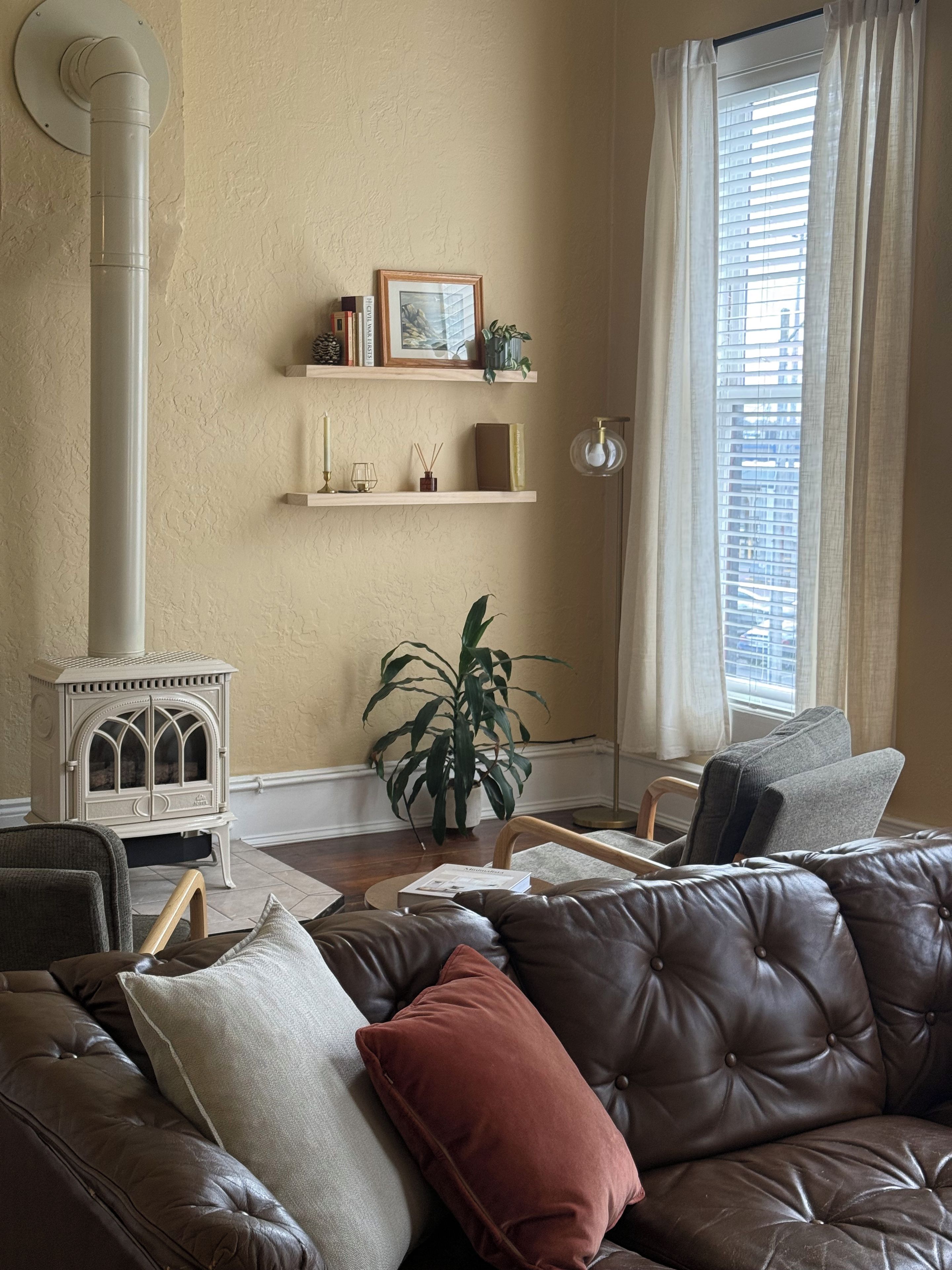 A cozy living room with a brown leather sofa, a white radiator, a potted plant, and a window with curtains.