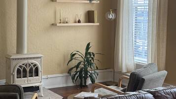 A cozy living room with a brown leather sofa, a white radiator, a potted plant, and a window with curtains.