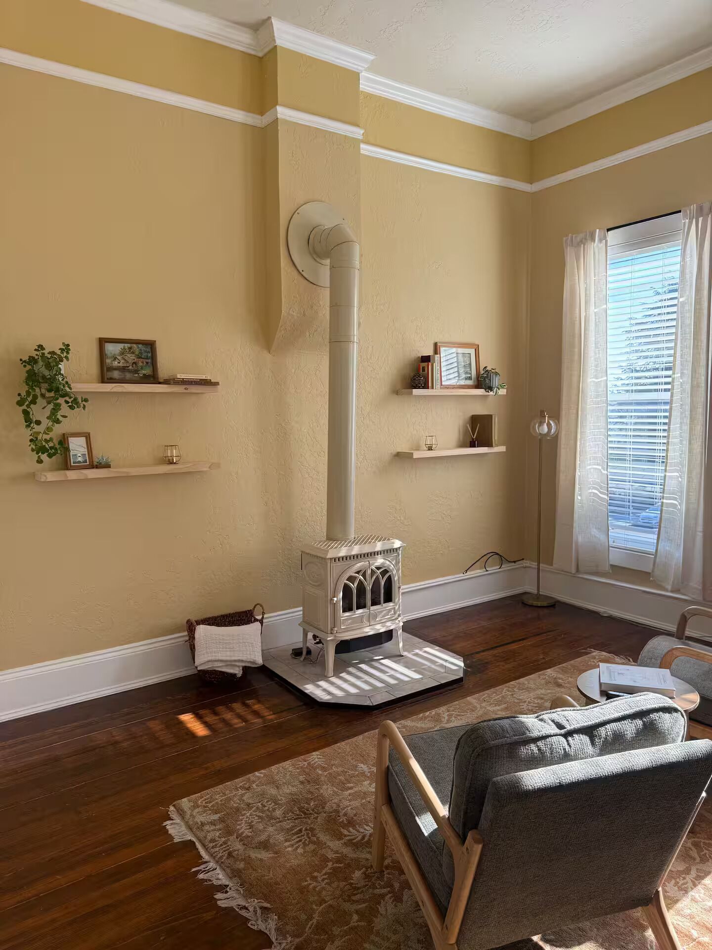 A living room with a wood-burning stove, a sofa, a floor lamp, and a window with blinds.