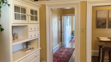 A hallway with wooden flooring, a white cabinet with glass doors, and a red patterned rug.