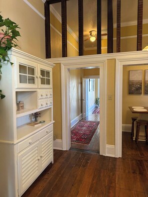 A hallway with wooden flooring, a white cabinet with glass doors, and a red patterned rug.