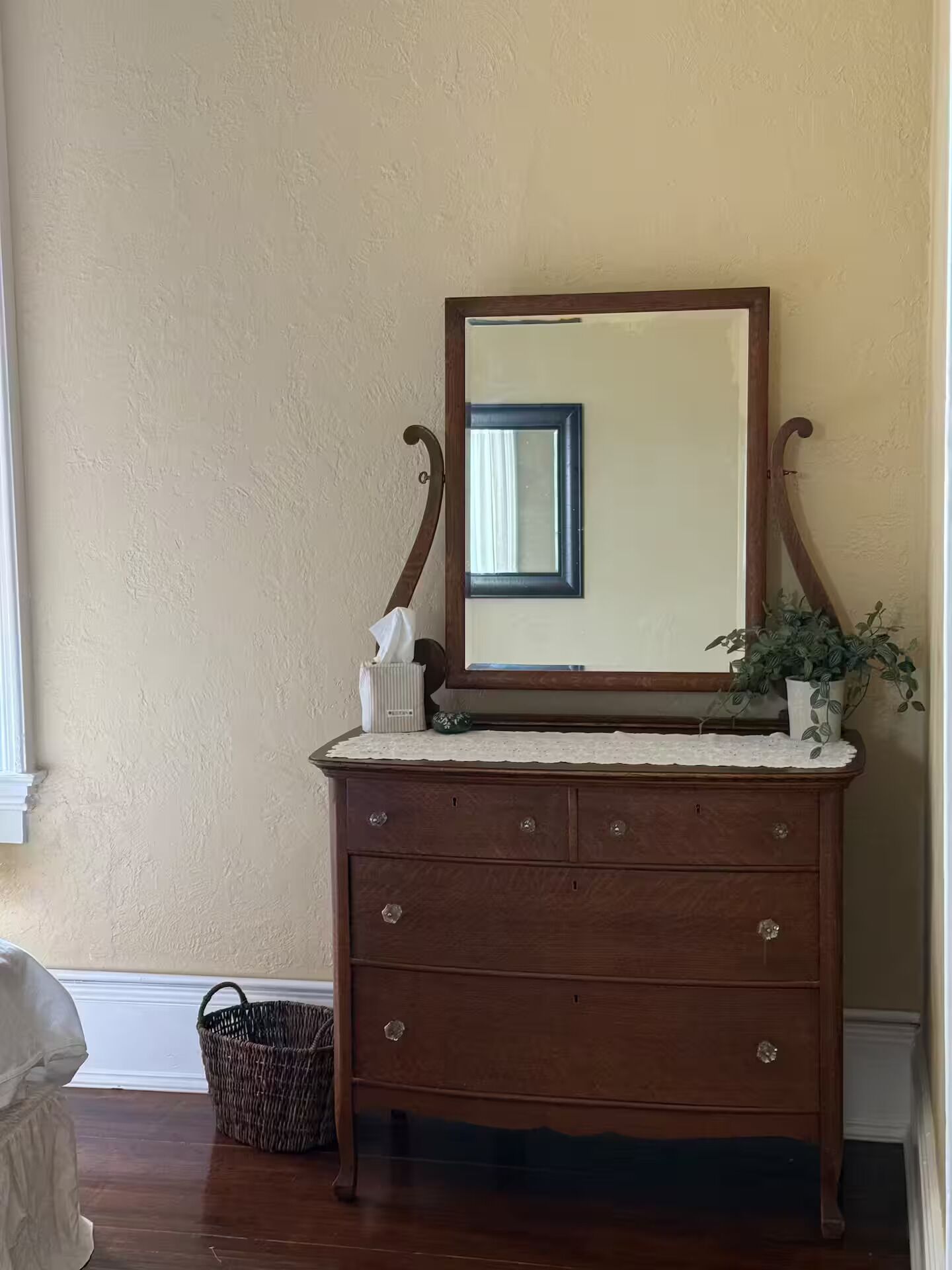 A wooden dresser with a mirror, a tissue box, and a plant.