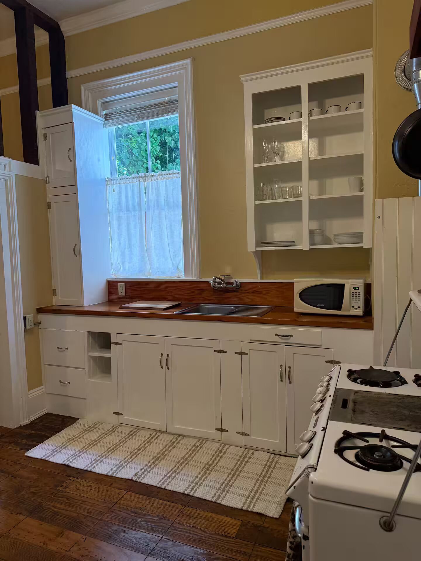 A kitchen with white cabinets, a microwave, a stove, and a window with curtains.