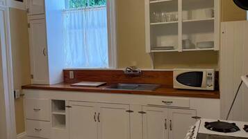 A kitchen with white cabinets, a microwave, a stove, and a window with curtains.