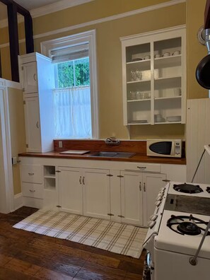 A kitchen with white cabinets, a microwave, a stove, and a window with curtains.