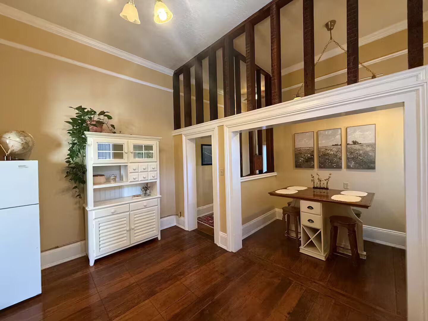 A kitchen with wooden flooring, a white refrigerator, a built-in cabinet, and a dining area with a table and chairs.