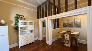 A kitchen with wooden flooring, a white refrigerator, a built-in cabinet, and a dining area with a table and chairs.