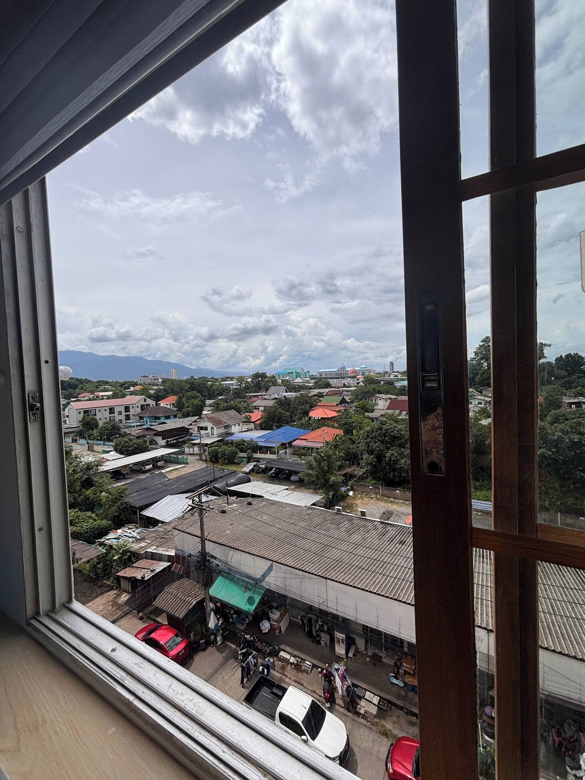 A view from a window overlooking a residential area with houses, a small market, and a distant mountain range.