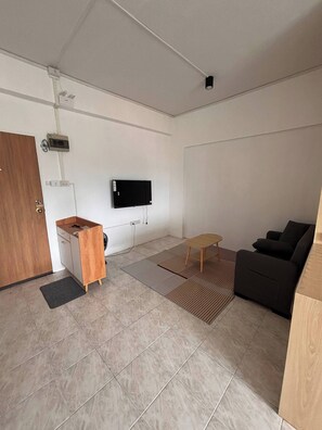A modern living space with a flat-screen TV mounted on the wall, a wooden desk with a chair, a sofa, and a small table. - Cosy Studio, Mountains View, Minutes to Everything (Chiang Mai)