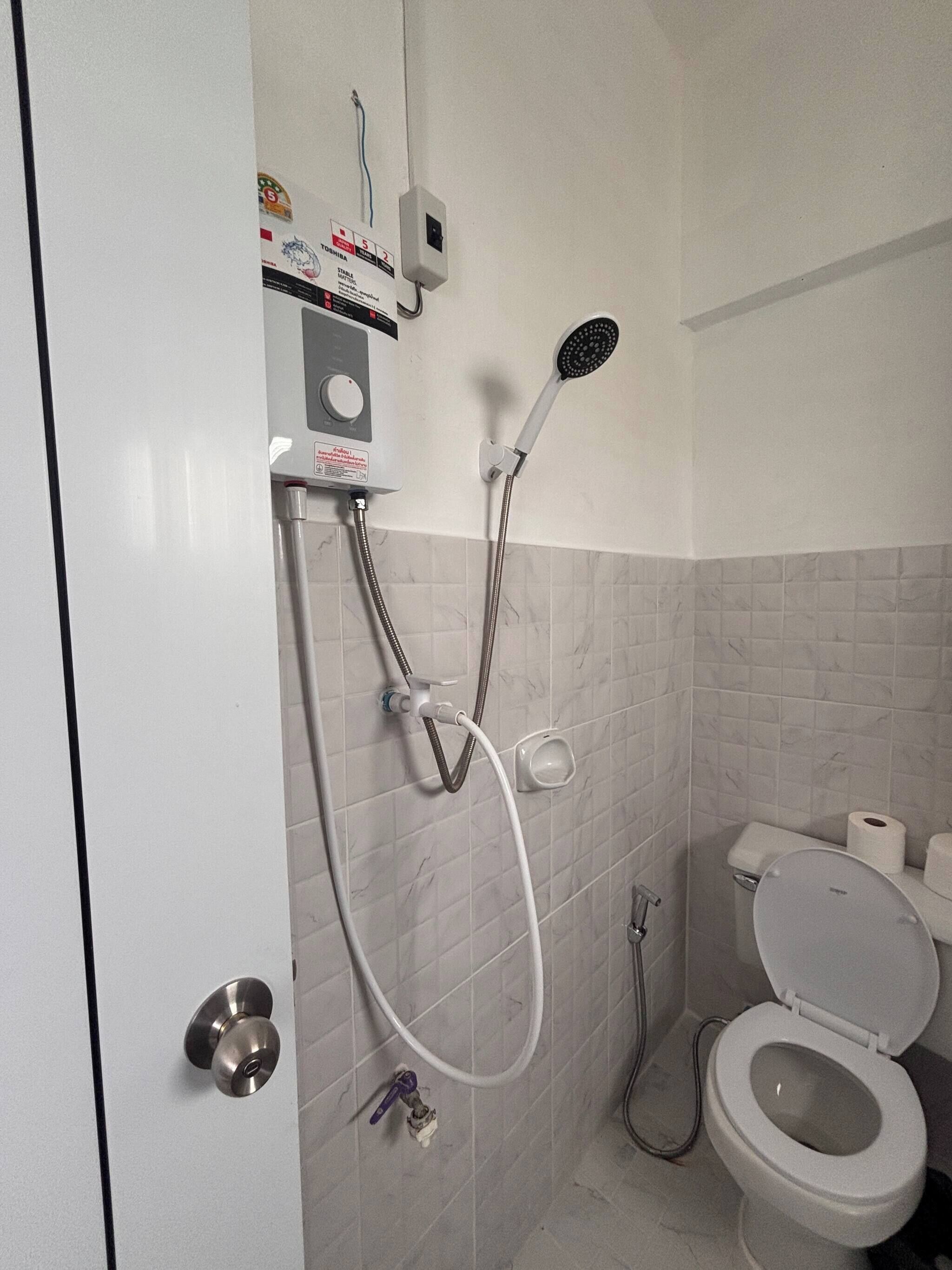 Un baño con inodoro, ducha con cabezal de ducha manual y panel de control en la pared.