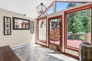 A sunlit room with a stone floor, large windows, and a wooden deck visible through the glass doors.