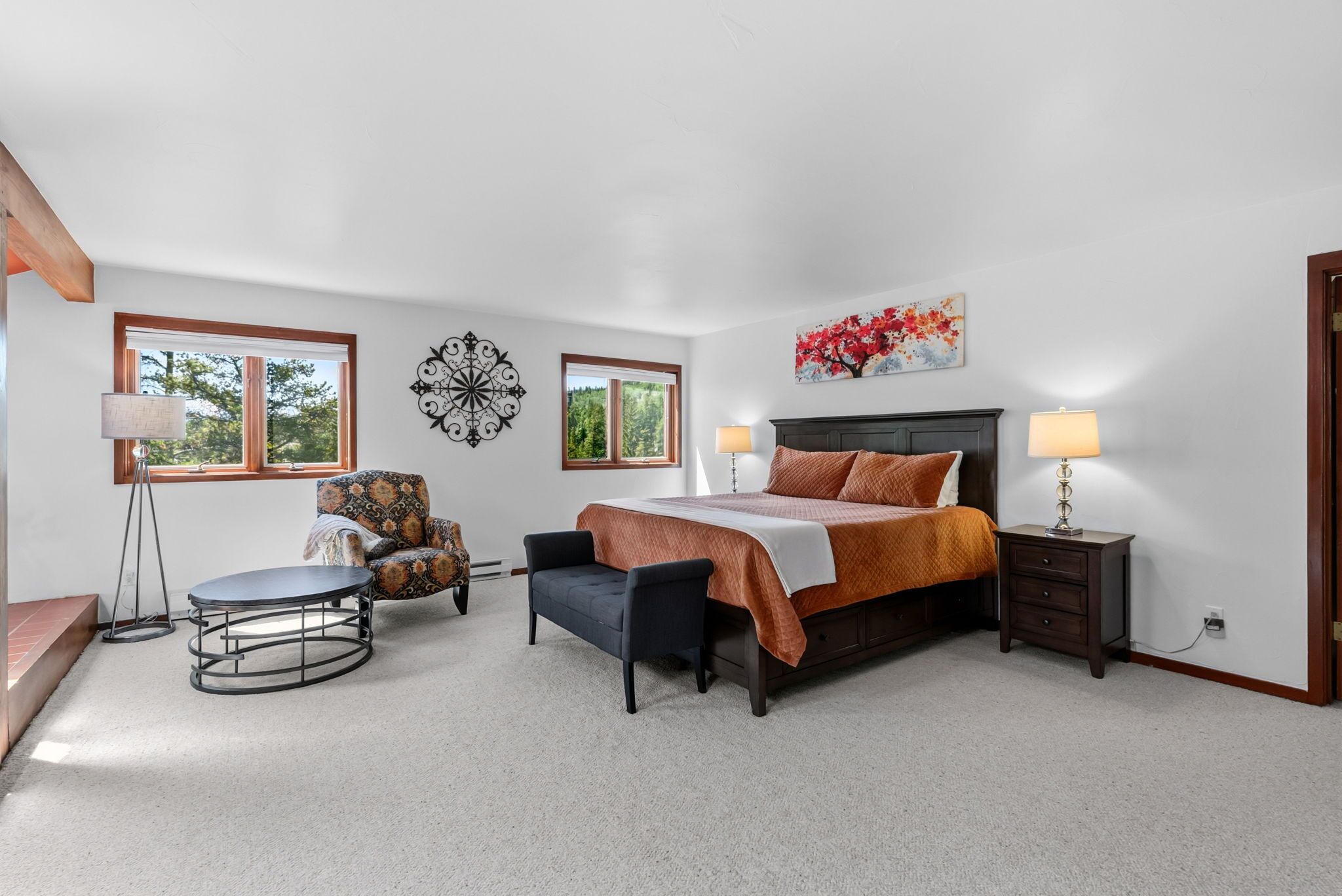 A bedroom with a bed, two bedside lamps, a chair, a round table, and a wall clock.