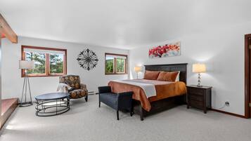 A bedroom with a bed, two bedside lamps, a chair, a round table, and a wall clock.